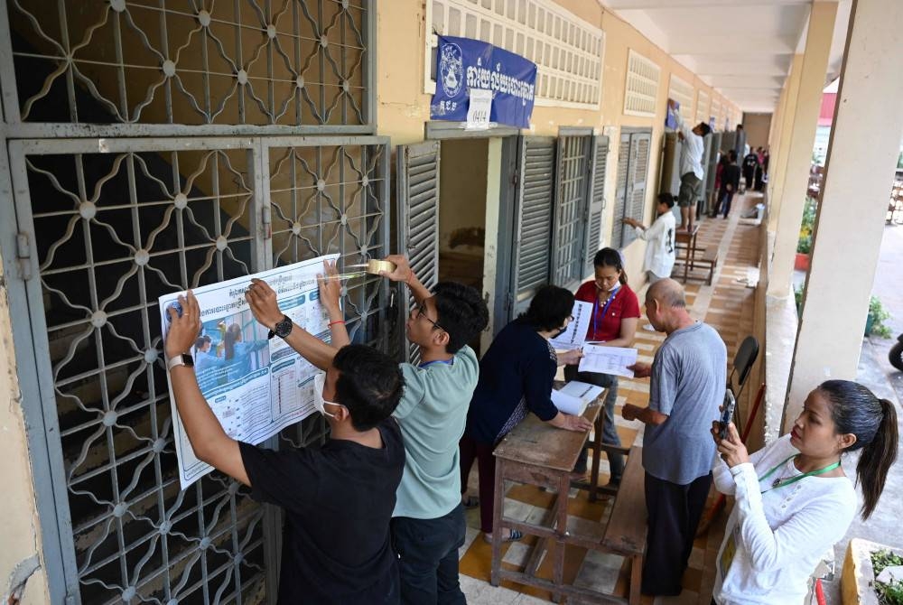 Pegawai pilihan raya umum menyediakan poster informasi di sebuah pusat mengundi di Phnom Penh. - AFP