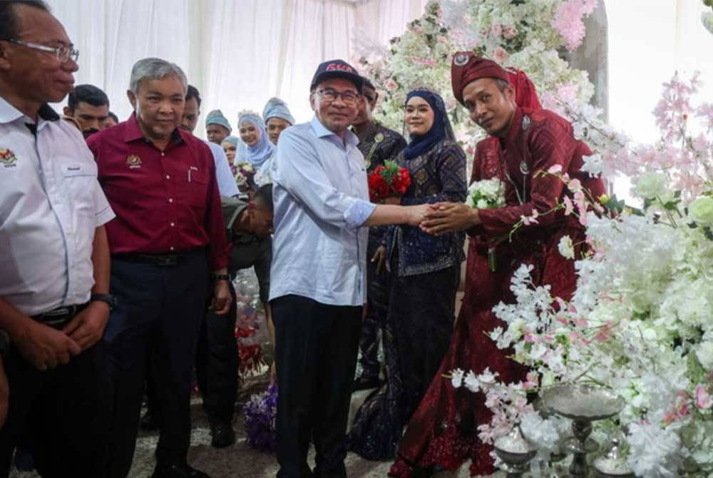 Anwar (tiga dari kiri) beramah mesra bersama pengantin bagi Program Jom Kahwin pada Program Sentuhan Kasih Desa Madani Negeri Kelantan di Dataran Kesedar Paloh 2 pada Ahad. - Foto Bernama