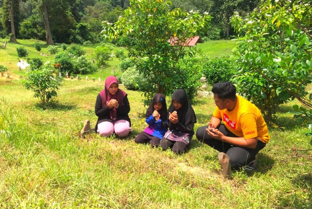 Nuriman Hakim (kanan) bersama Nur Amalyn (dua dari kanan), Nur Ilya Akma (tiga dari kanan) dan Nor Izyani (kiri) membacakan doa di kubur bapa mereka di Sungai Sam, Kuala Krai.