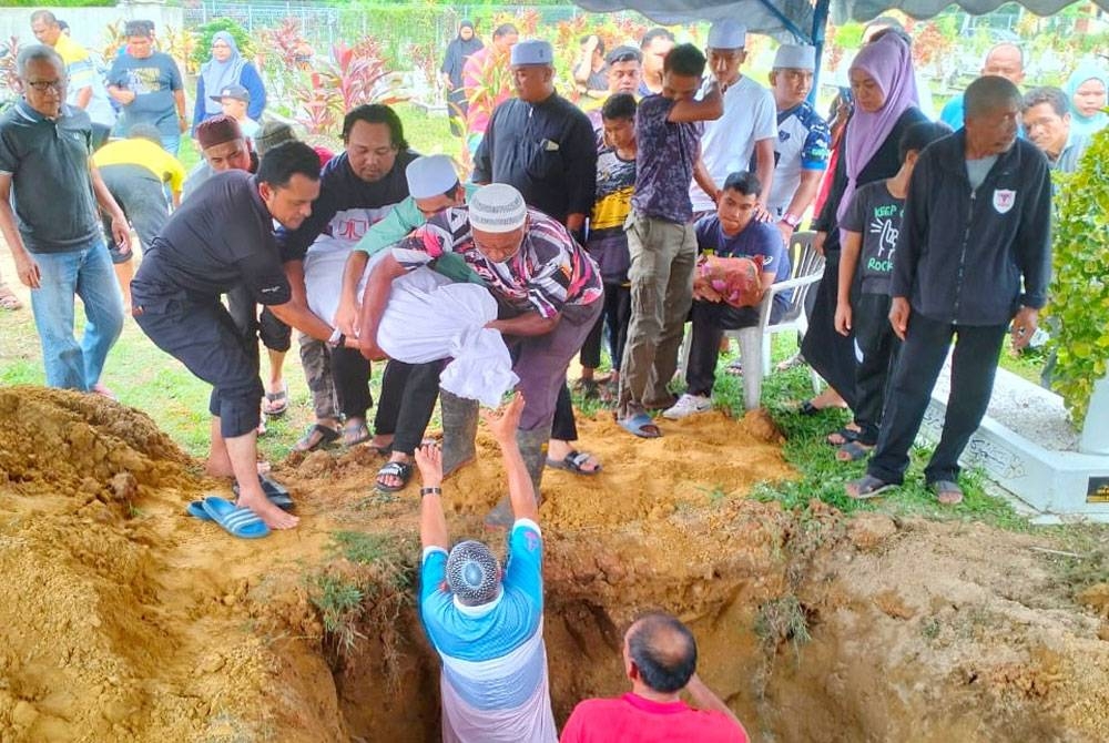 Zulhilmi memangku jenazah bayinya berusia dua bulan sambil melihat pengebumian jenazah isteri di Kampung Semat Jal, Tumpat.