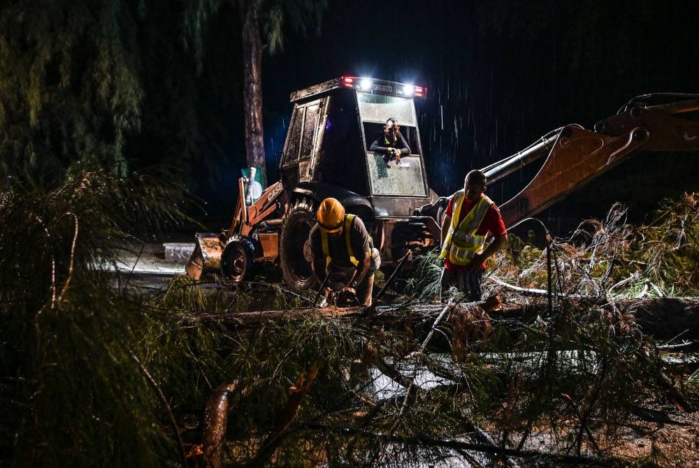 Pekerja kontraktor melakukan kerja-kerja mengalihkan dan membersihkan pokok-pokok yang tumbang dalam kejadian hujan lebat dan ribut ketika tinjauan di sekitar Pantai Teluk Ketapang Rabu. - Foto Bernama