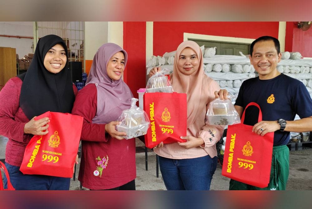 Sayani (dua dari kiri) menyerahkan agihan bubur asyura kepada wartawan Utusan Malaysia, Asliza Musa pada program Bubur Asyura anjuran Bomba Perak di Ipoh.