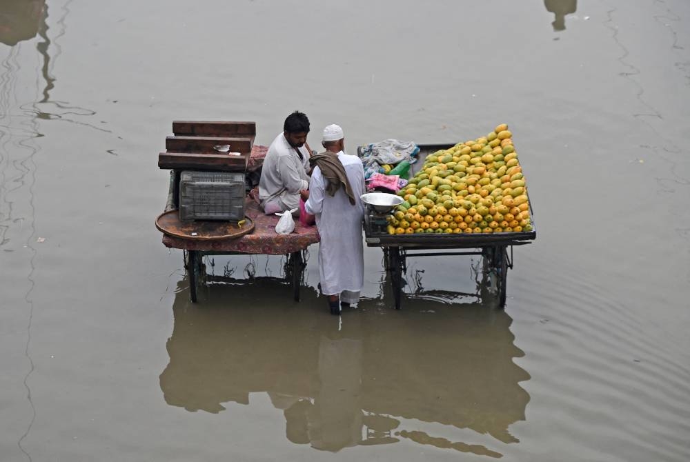 Peniaga terpaksa menjual buah-buahan walaupun banjir melanda jalan raya di Karachi. - Foto AFP