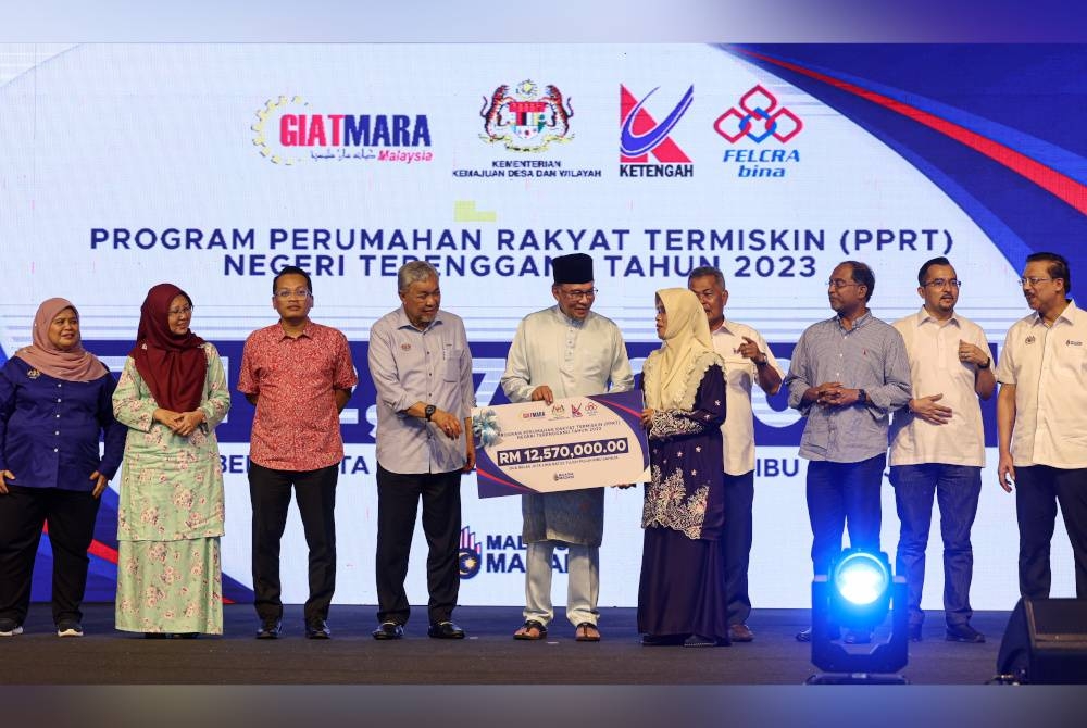 Anwar (tengah) menyampaikan replika cek Program Perumahan Rakyat Termiskin (PPRT) Negeri Terengganu 2023 kepada wakil penduduk pada Perasmian Sentuhan Kasih Desa Terengganu di Kompleks Sukan Ketengah, Bandar Al Muktafi Billah Shah, pada Jumaat. - Foto Bernama