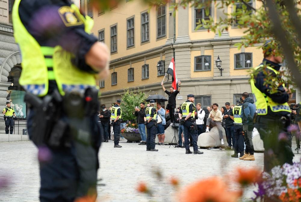 Anggota polis mengawal sekumpulan kecil bantah cemas al-Quran di dataran Mynttorget Stockholm, Sweden. - AFP