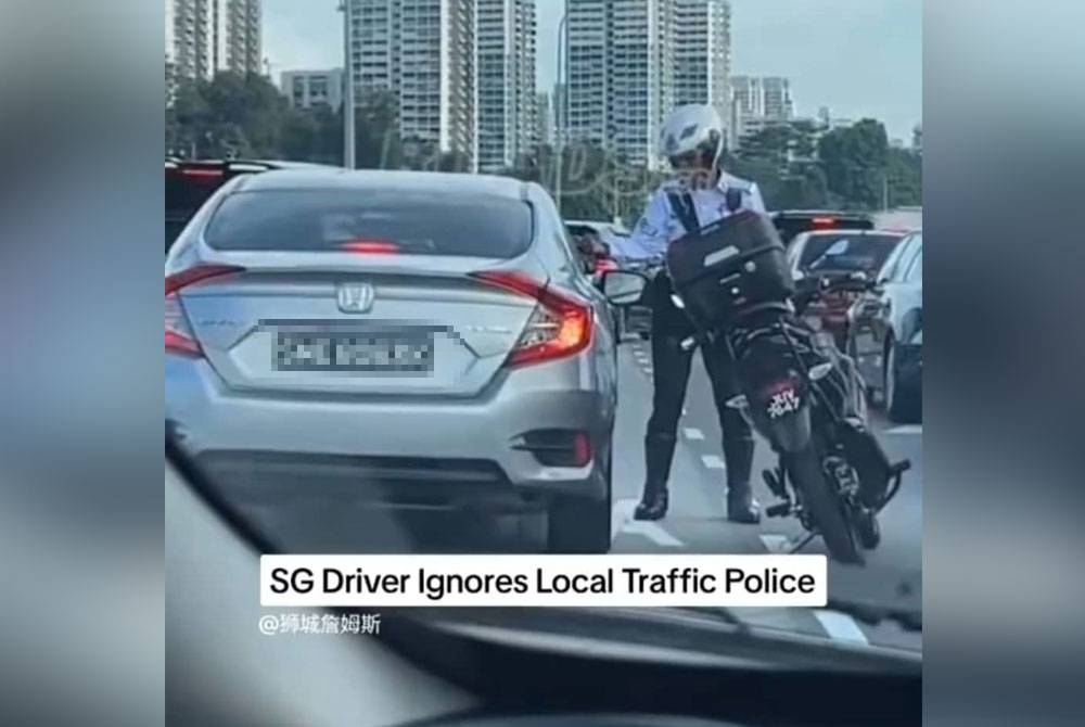 Tangkap layar menunjukkan seorang anggota polis trafik cuba menghalang sebuah kereta dengan nombor pendaftaran Singapura daripada meneruskan perjalanan di BSI, Johor Bahru.