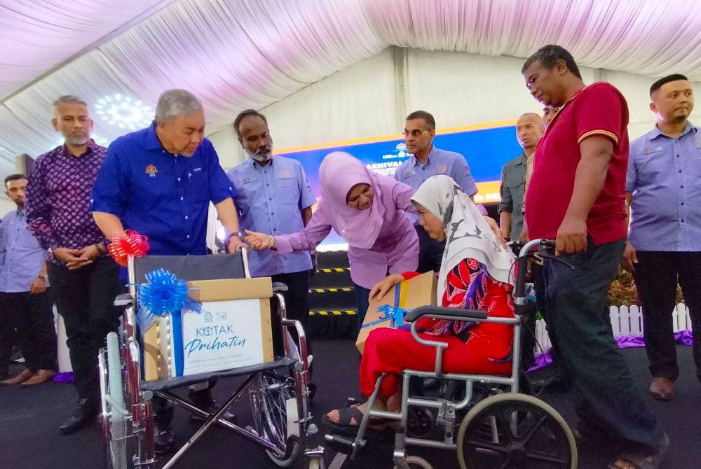 Ahmad Zahid (kiri) menyampaikan bantuan faedah PERKESO kepada salah seorang pencarum pada Karnival Kerjaya MyFutureJobs bersama HAWA di Kepala Batas pada Sabtu.