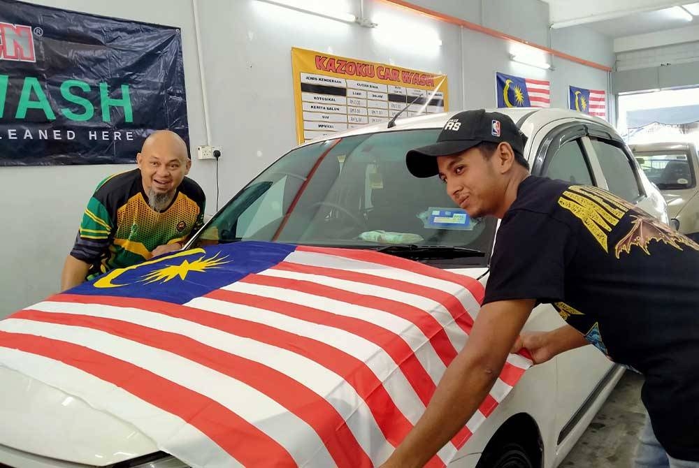 Abdul Salim (kiri) menyerahkan Jalur Gemilang kepada salah seorang pelanggannya di Pusat Cucian Kenderaan Kazoku di Pekan Razaki di sini pada Ahad.