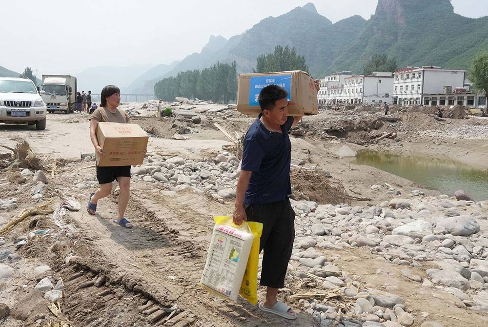 Penduduk kampung membawa barangan bantuan di Kampung Shangzhuang di Bandar Sanpo, Kaunti Laishui, Wilayah Hebei utara China yang terjejas akibat hujan lebat. - Foto Xinhua