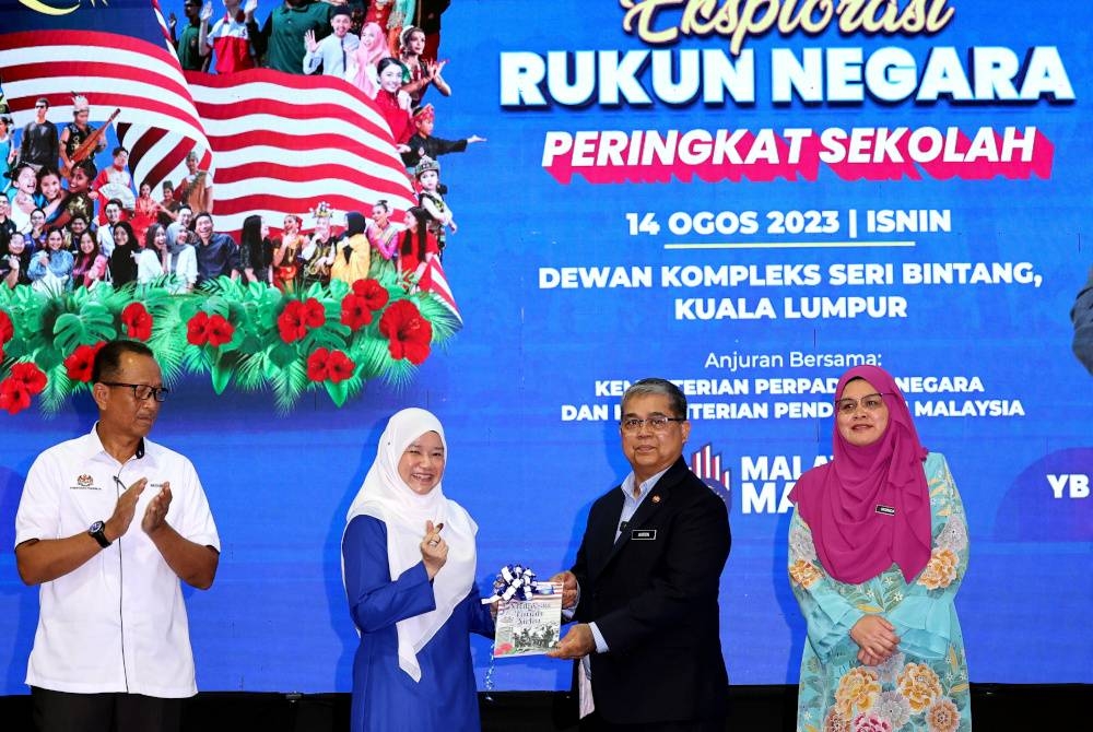 Aaron Ago Dagang menyerahkan buku “Malaysia Tanah Airku” kepada Fadhlina pada pelancaran program Eksplorasi Rukun Negara Peringkat Sekolah di Dewan Kompleks Seri Bintang di sini, pada Isnin. - Foto Bernama