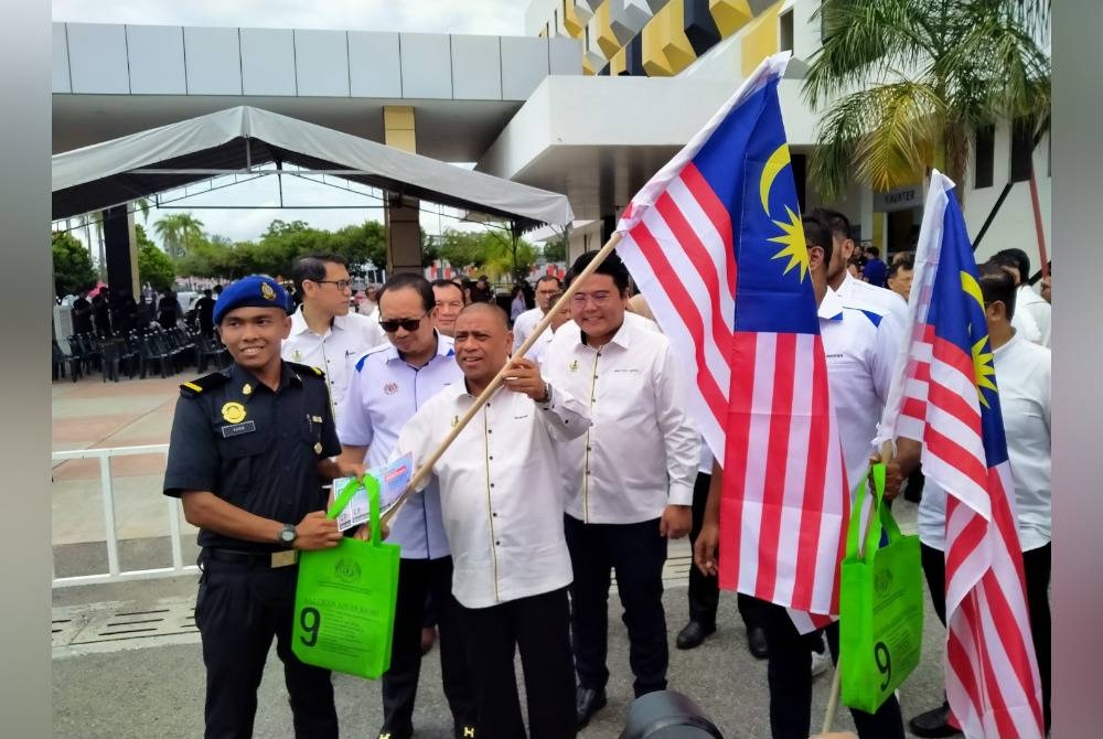 Saarani (depan, kanan) membuat penyerahan Jalur Gemilang kepada peserta Program Jelajah Pengguna-Peniaga Merdeka di pekarangan Stadium Indera Mulia pada Rabu.