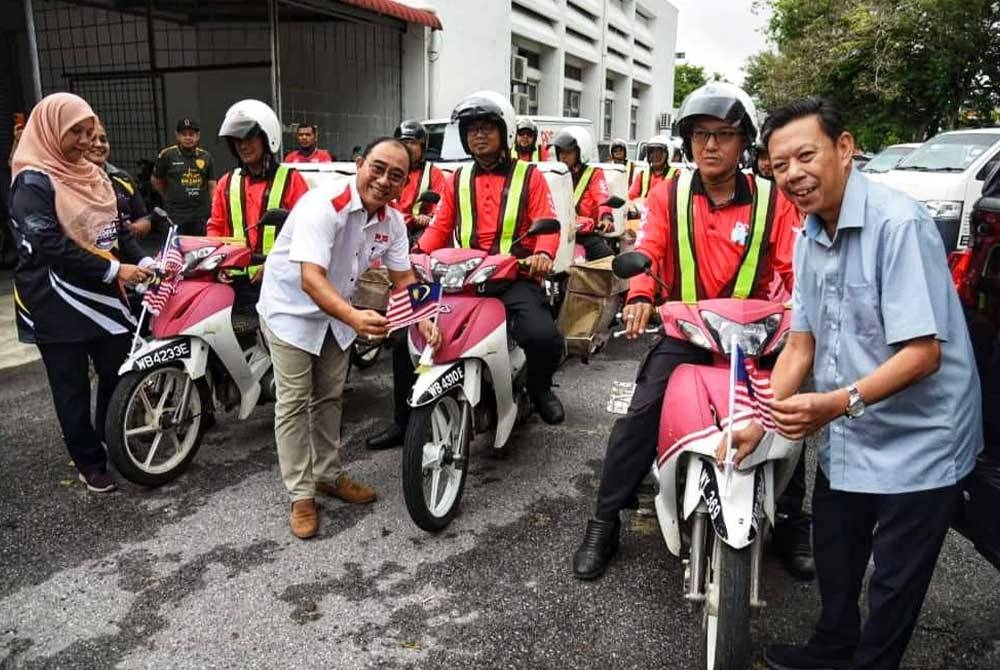 Nasrudin (kanan) melekatkan bendera pada motosikal posmen sempena Sambutan Hari Kebangsaan 2023.