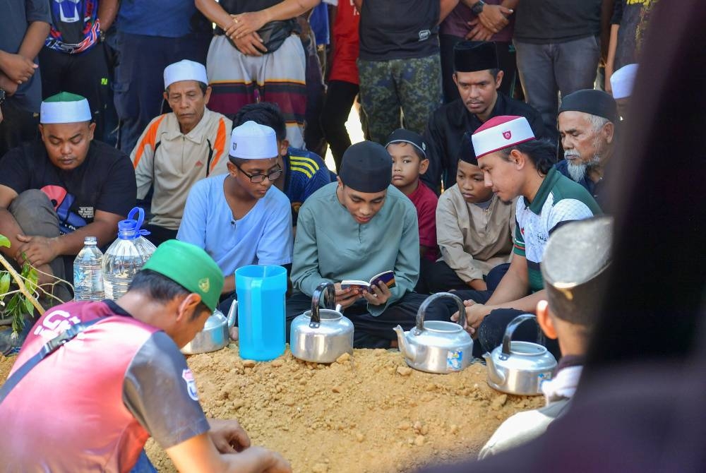 Khairul Harisin (tengah) mengetuai bacaan talkin di pusara bapanya yang menjadi mangsa nahas pesawat terhempas di Elmina selepas selesai upacara pengebumian di Tanah Perkuburan Felda Mempaga 1 hari ini. - Foto Bernama