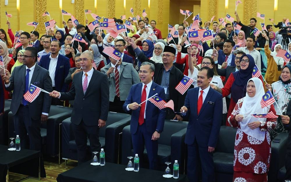 Fahmi (tengah) mengibarkan Jalur Gemilang sempena Bulan Kebangsaan dan Kibar Jalur Gemilang 2023 pada Perhimpunan Bulanan KKD di Kementerianya pada Isnin. - Foto: Bernama