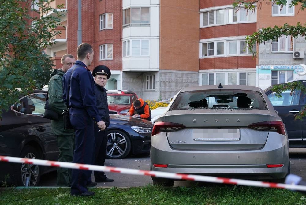 Pegawai penguat kuasa undang-undang berdiri di sebelah kereta yang rosak berikutan serangan dron di Krasnogorsk, Moscow. - Foto AFP