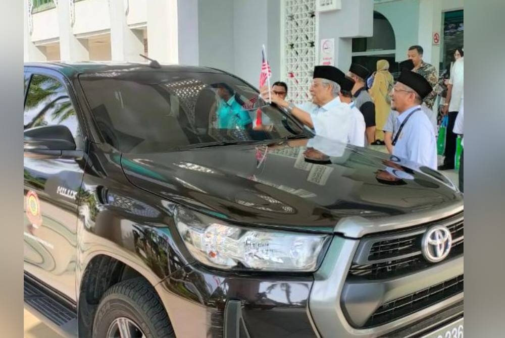 Abdul Aziz (dua dari kanan) melekatkan Jalur Gemilang pada sebuah kereta sebagai simbolik penyerahan Jalur Gemilang di Bangunan Sultan Idris Shah, Shah Alam pada Isnin.