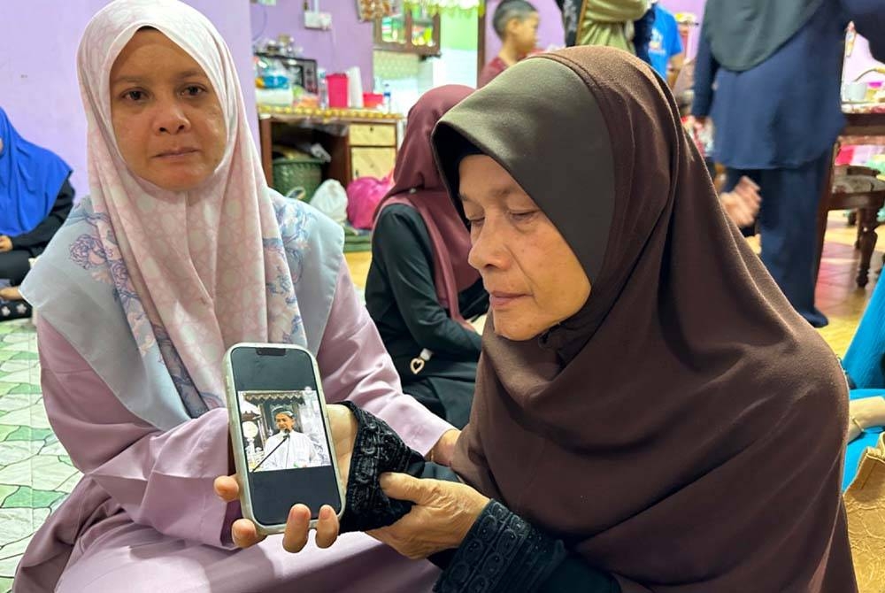 Robiah (kanan) menunjukkan gambar arwah suaminya ketika membaca khutbah sebelum ini.