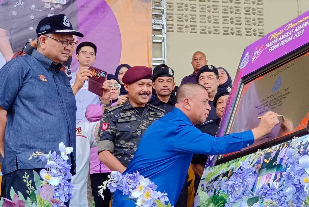 Saarani menandatangani plak simbolik merasmikan Taman Angkat Amanita Taman Bukit Senyum, Lenggong sambil diperhatikan oleh Mohd Yusri (tengah) di Stadium Mini Lenggong pada Sabtu.