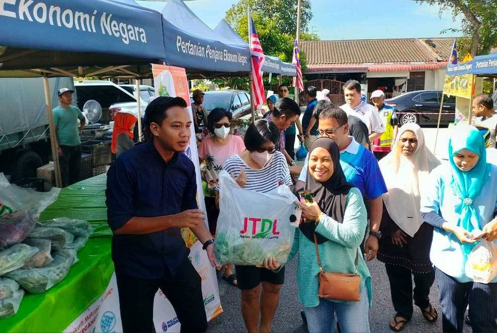 Fahmi (kiri) mengedarkan sayur percuma pengunjung Program Jualan Agro Madani di kawasan Dewan Undangan Negeri (DUN) Pantai Jerejak pada Ahad.