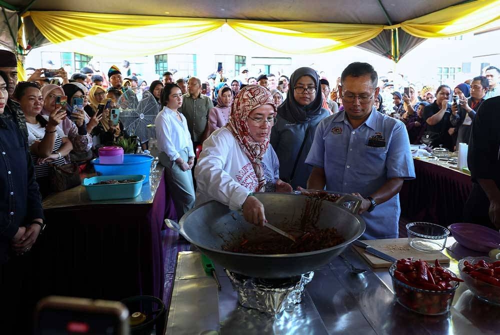 Tunku Azizah berkenan memasak sambal ikan bilis berlada sewaktu tiba pada program Santapan Rakyat di Dewan Perdana hari ini. - Foto Benama