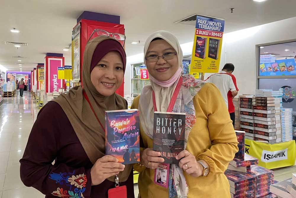 Mazuen (kiri) menunjukkan novel bertajuk Bawah Payung Awan karya Liza Nur dan Shahida pula memegang novel Bitter Honey yang merupakan antara buku baharu diterbitkan sempena Jualan Gudang Karangkraf 2023.