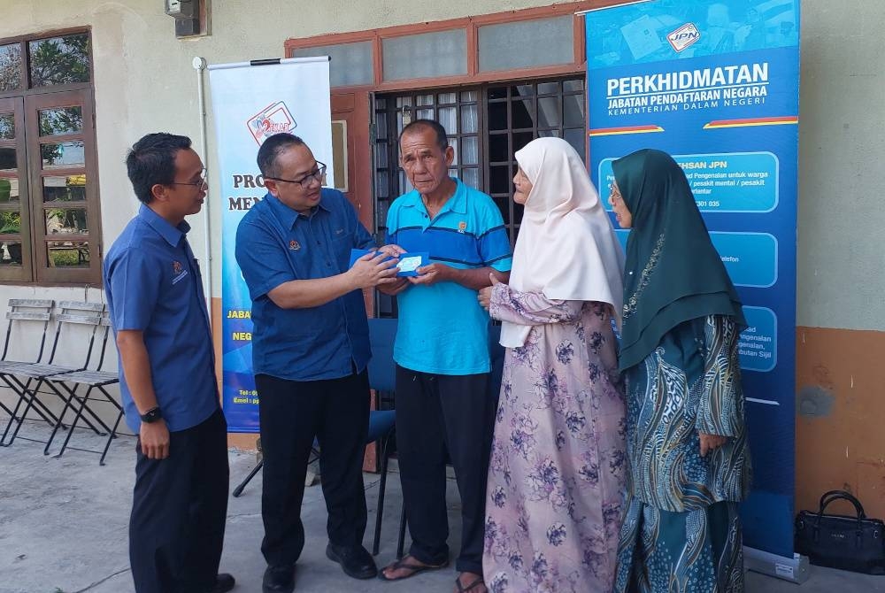 Ketua Pengarah Jabatan Pendaftaran Negara (JPN), Zamri Misman (dua dari kiri) menyerahkan MyKad kepada Abdul Wahab (tengah)