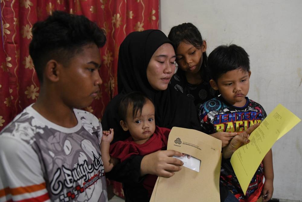 Nur Ammera melihat surat bantuan PERKESO yang diterima bersama anak-anaknya Izzdanish,14, (kiri), Fatima Alyysa Muhammad Firdaus, sembilan bulan, (dua dari kiri), Aqeel Mikhael,4, (kanan) dan Dahlea Amanda,8, (dua dari kanan) di kediamannya di Machang Bubok, pada Jumaat. - Foto Bernama