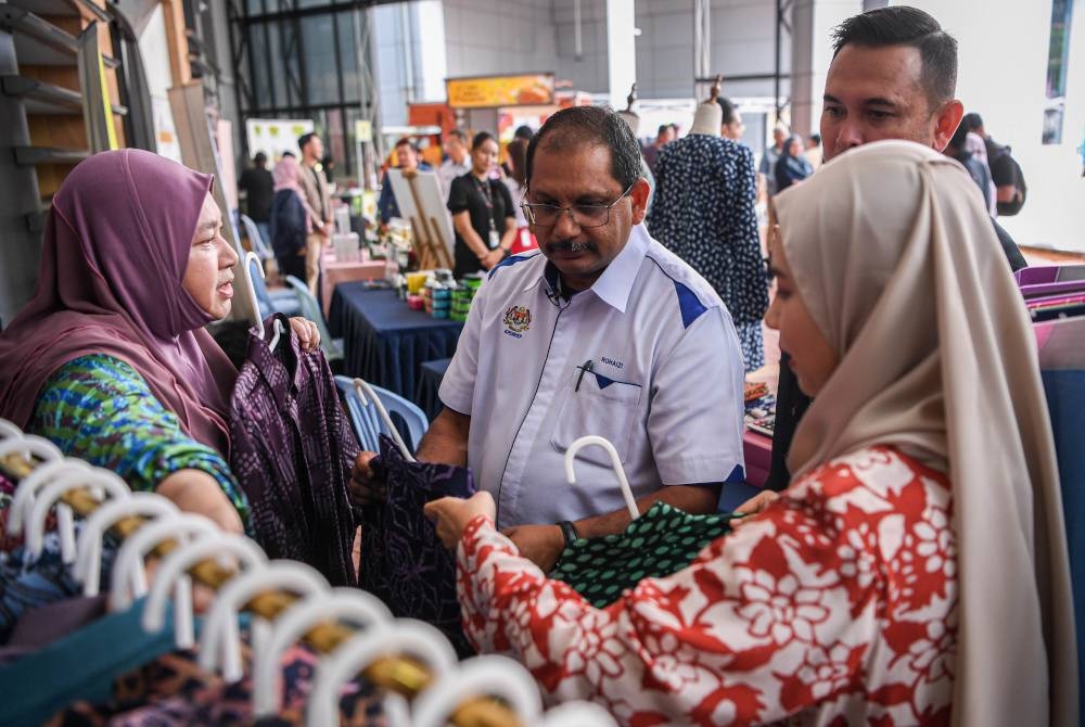 Rohaizi (dua, kiri) mendengar penerangan daripada Pengurus Ruzima Batik, Wan Ruzima Wan Abdullah (kiri) berhubung batik asli buatan Terengganu pada Majlis Pra-Pelancaran Kempen Beli Barangan Malaysia 2023 pada Rabu. - Foto Bernama