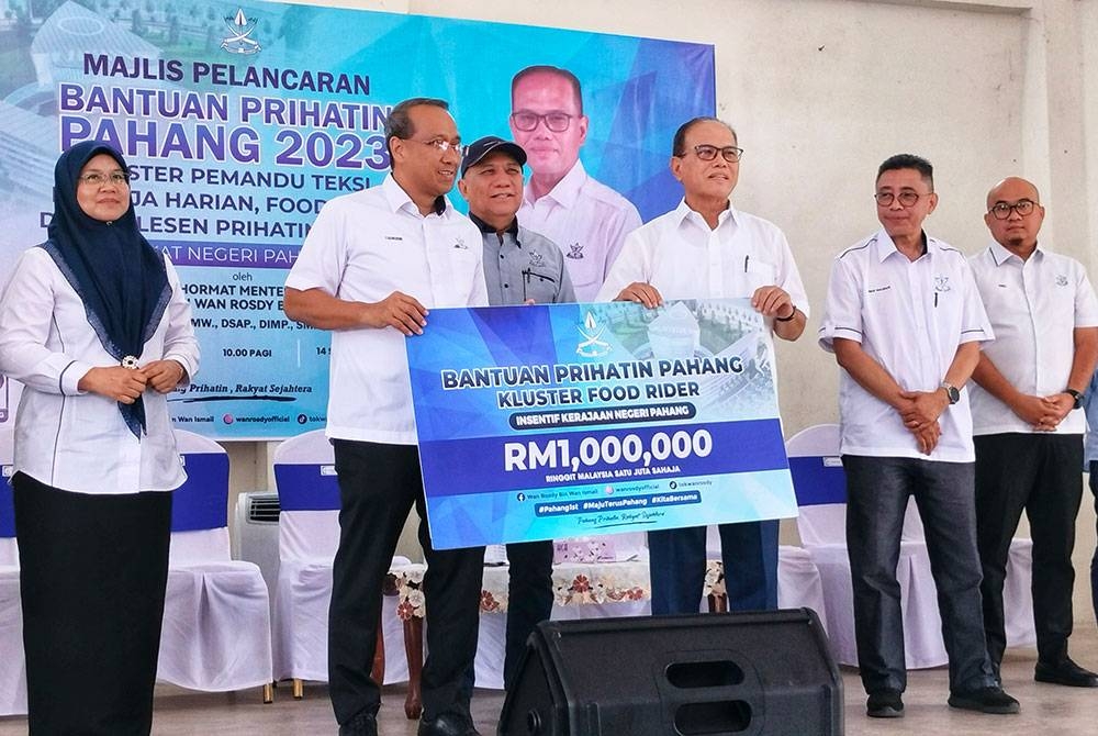 Wan Rosdy (empat dari kanan) menyerahkan replika cek BBP 2023 kluster penghantar makanan kepada Exco Kerja Raya, Pengangkutan dan Kesihatan Pahang, Datuk Mohammad Fakhruddin Mohd Ariff(tiga dari Kiri) dalam majlis pelancaran program itu di Dewan Orang Ramai Agropolitan Felda Chemomoi, Bentong pada Khamis.