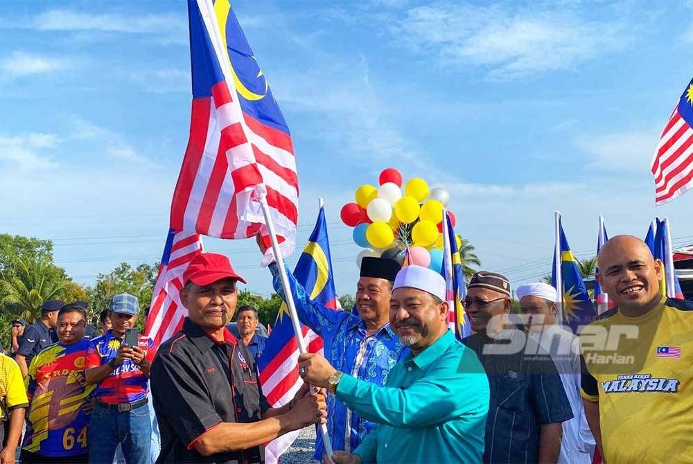 Mohd Nassuruddin (dua, kanan) menyerahkan Jalur Gemilang kepada Mohd Yunus Musa semasa Program Semarak Hari Kebangsaan dan Hari Malaysia Peringkat Kawasan Rukun Tetangga (KRT) Pasir Mas di Meranti.