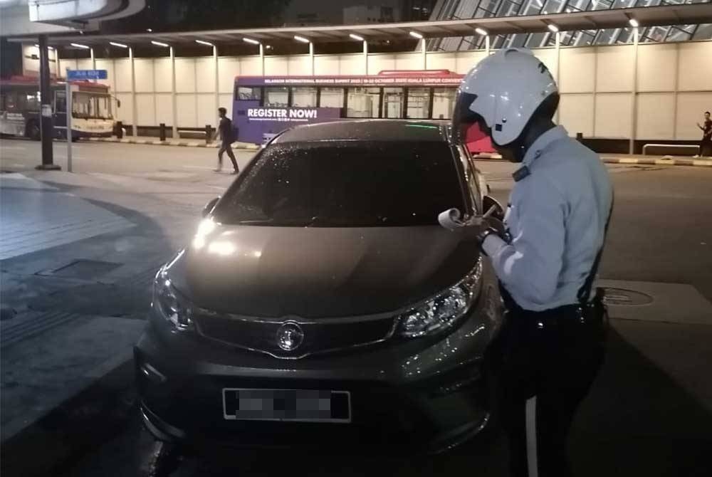 Anggota polis trafik bertindak mengeluarkan saman kepada pengguna jalan raya yang masih tidak mematuhi peraturan lalu lintas.