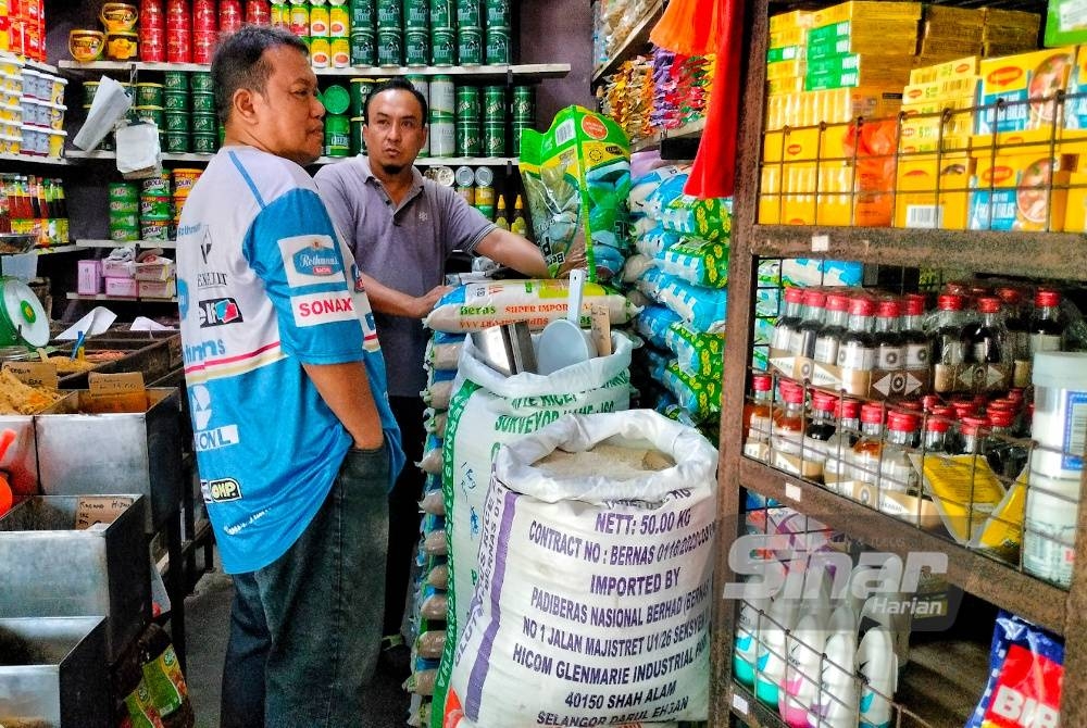 Mohd Nazri (dua, kiri) ketika sedang melayan pelanggan yang mahu membeli beras di kedai runcitnya di Pasar Awam Bachang pada Selasa.
