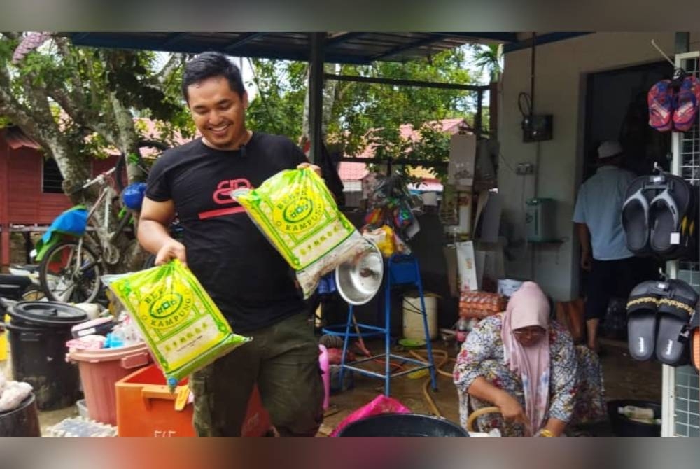 Muhamad Amirul menunjukkan beras yang terpaksa dilelong kerana rosak akibat terkena air banjir di Kampung Charuk Akar, Mukim Tawar pada Khamis.