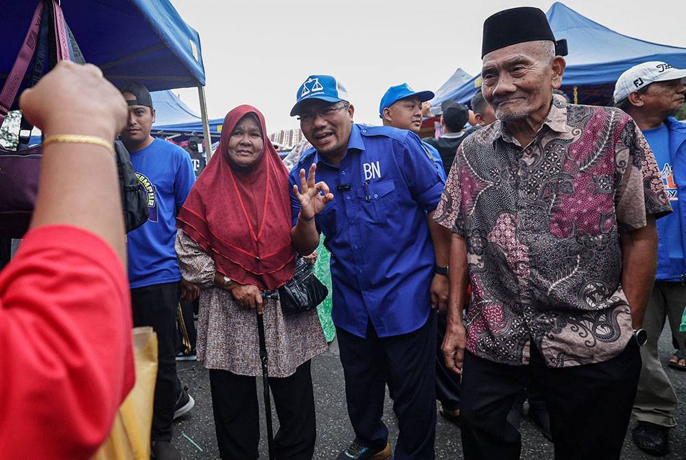 Amizar bersama ayahnya Abu Adam (kanan) beramah mesra bersama pengunjung di tapak pasar malam Felda Chemomoi pada kempen PRK DUN) Pelangai. - Foto Bernama