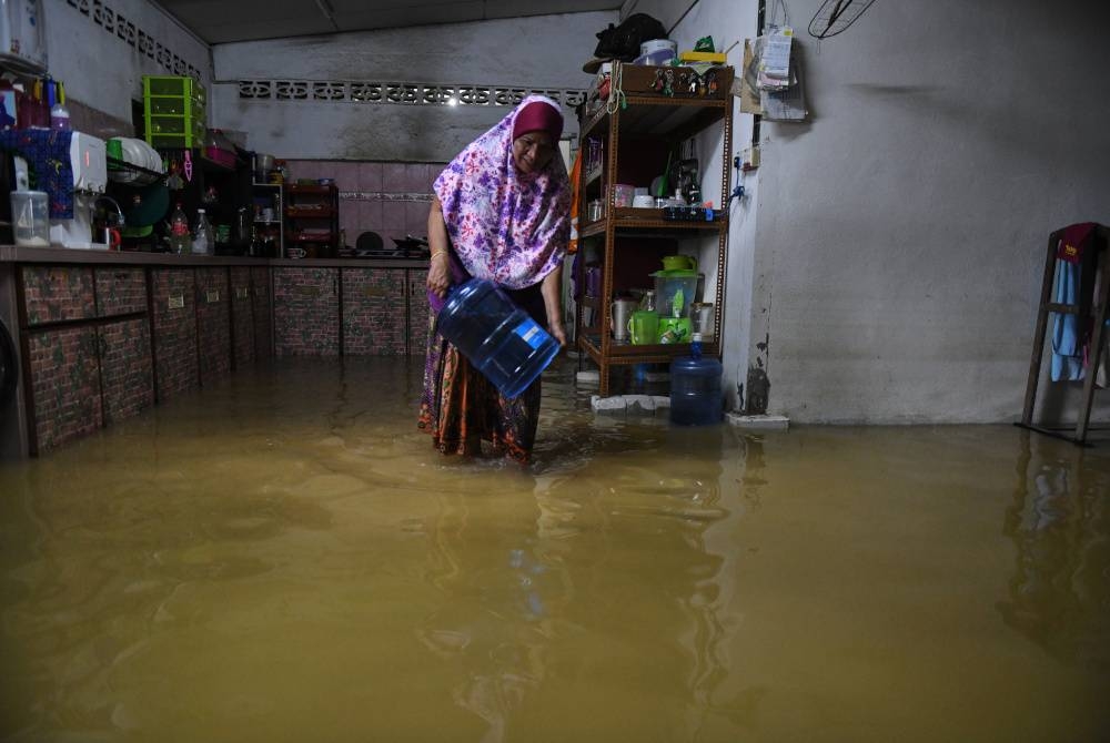 Suri rumah, Azizah Rehab, 62, menyelamatkan barang-barang keperluan harian apabila rumahnya di Jalan Kampung Masjid, Teluk Kumbar dinaiki air. - Foto Bernama