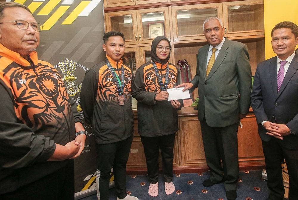 Khairudin (dua dari kanan) menyampaikan sumbangan kepada Aleena dan Izzat yang memenangi pingat di Kejohanan Dunia Boling Padang di pejabatnya di sini pada Selasa.