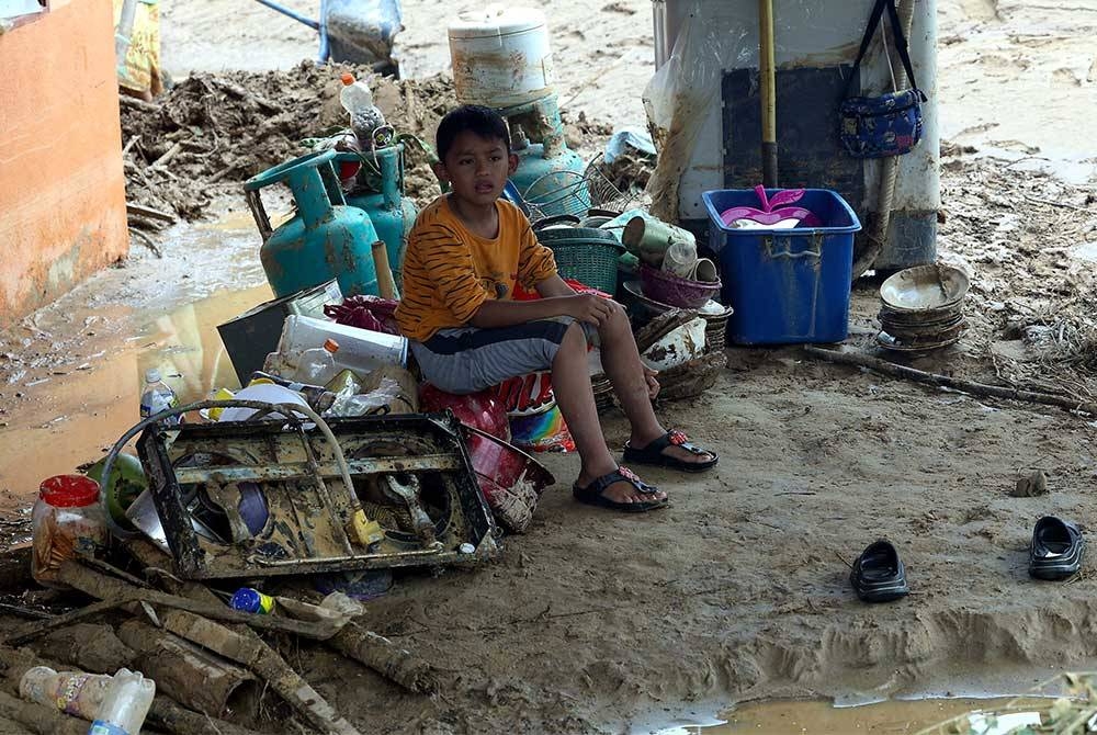 Seorang kanak-kanak berehat seketika selepas membantu keluarganya membersihkan rumah di Kampung Padang Empang yang ditenggelami air. - Foto Bernama