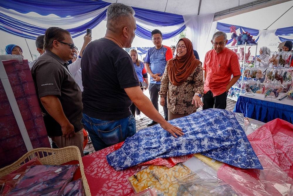 Fuziah (tengah) mendengar penerangan yang disampaikan oleh pembuat Batik Clay Azmeer Zaharin, 45, (dua, kiri) semasa melawat reruai jualan produk tempatan selepas merasmikan Program Jelajah Jualan Rahmah Peringkat Pegeri Melaka di Dataran Sejarah dekat Ayer Keroh hari ini. Foto Bernama