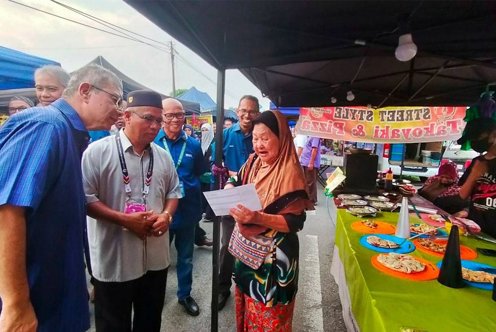 Saifuddin (kiri) menemani calon PN, Cikgu Kasim ketika berkempen di pasar malam Felda Chemomoi di sini.