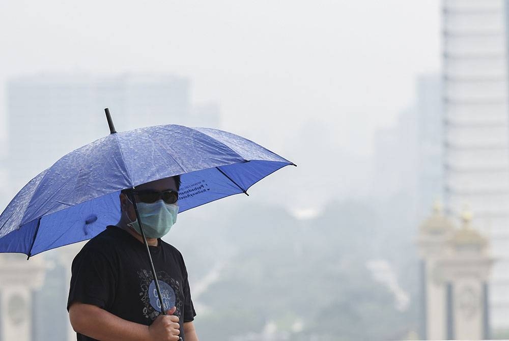 Seorang pemuda memakai pelitup muka dan berpayung ketika lalu di kawasan Pusat Pentadbiran Kerajaan di Putrajaya yang diselubungi jerebu disertai hujan renyai pada tinjauan di Presint 5 hari ini. Foto Bernama