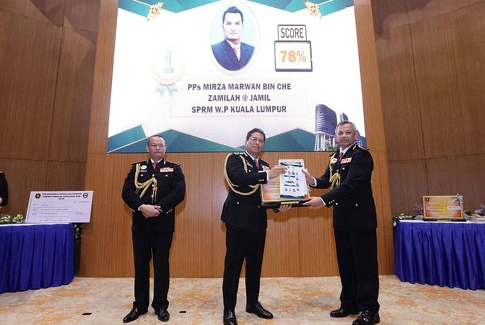 Azam (tengah) menyampaikan hadiah pemenang tempat pertama reka bentuk setem kepada Pengarah SPRM Kuala Lumpur, Datuk Mohamed Fauzi Husin (kanan) sambil disaksikan oleh Pengarah Bahagian Dasar, Perancangan dan Penyelidikan SPRM, Datuk Mohd Hafaz Nazar.