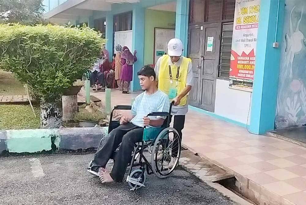 Petugas SPR menolak kerusi Amim Fiktri bagi membolehkan dia membuang undi di saluran tiga di Pusat Mengundi SMK Seri Pelangai pada Sabtu.