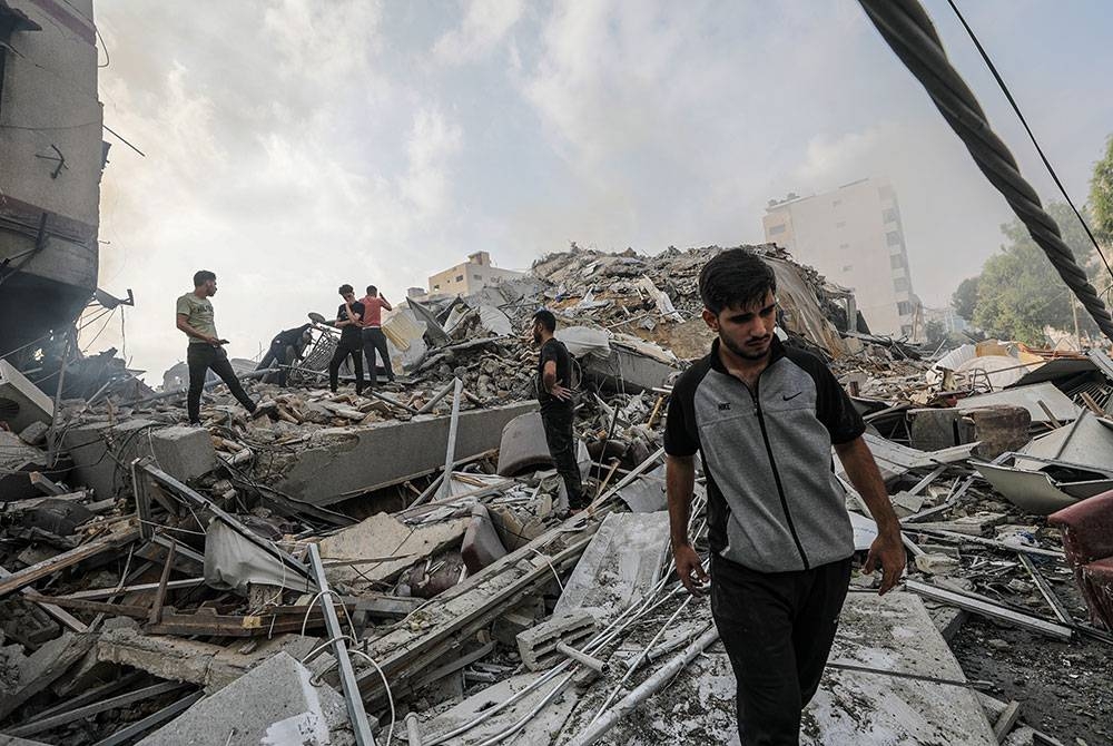 Penduduk Palestin memeriksa runtuhan rumah mereka yang musnah akibat serangan udara Israel berhampiran Menara Al-Watan di bandar Gaza. - Foto EPA