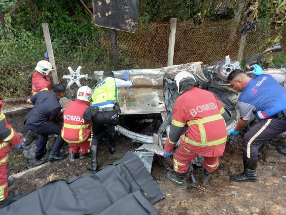 Anggota bomba dan polis berusaha mengalihkan kereta yang terbakar setelah terjatuh ke dalam cerun di Kilometer 290.4 Lebuhraya Utara Selatan (PLUS) arah Kajang pada Khamis. - Foto Jabatan Bomba dan Penyelamat Malaysia