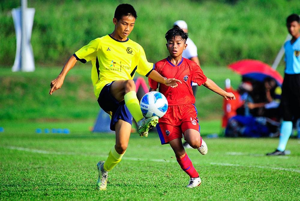 Aksi pemain AMD Dream (kanan) cuba mencabar bola daripada pemain Evergrande Football School pada aksi separuh akhir pada Jumaat.