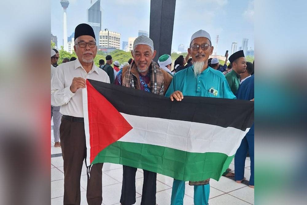 Hassan (kiri) mengibarkan bendera Palestin selepas perhimpunan menyokong rakyat Palestin di Masjid Negara Kuala Lumpur pada Jumaat.