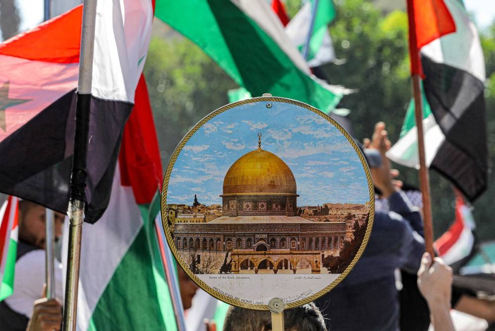 Seorang budak lelaki memegang papan tanda yang menunjukkan gambar Dome of the Rock di pekarangan Masjidil Aqsa di Baitulmaqdis, sambil dikelilingi bendera kebangsaan Palestin dan Syria semasa perhimpunan anti-Israel di Dataran Arnous tengah Damsyik pada Jumaat. - Foto AFP