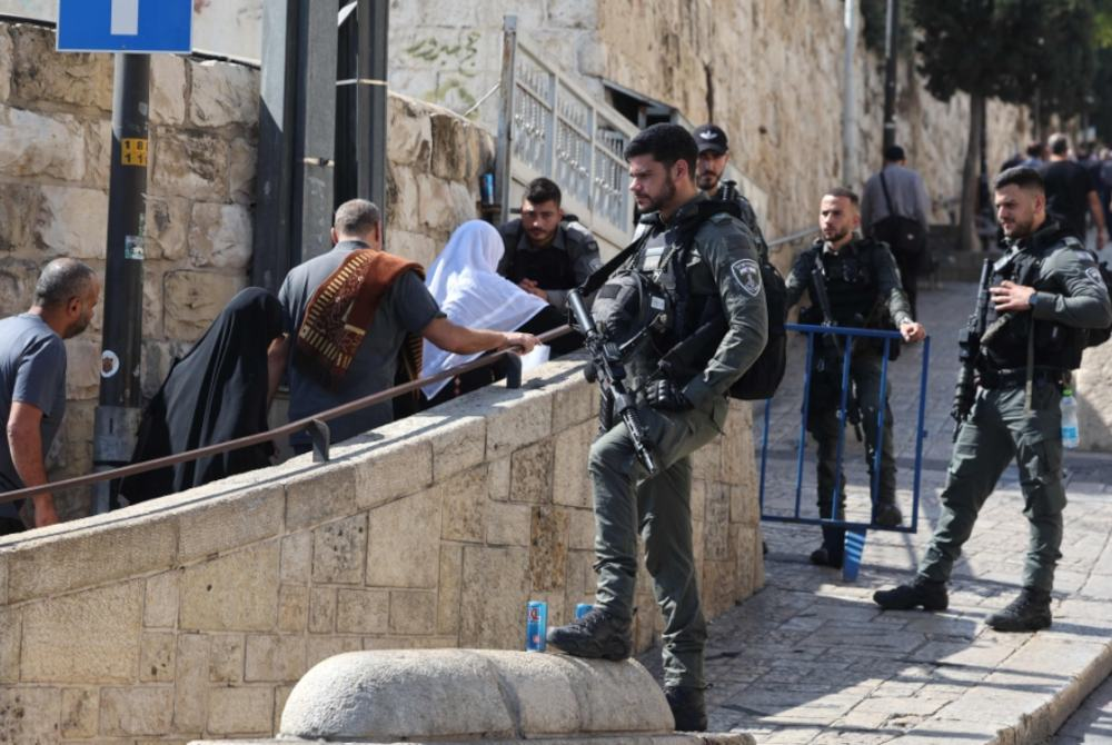 Anggota keselamatan Israel melihat penduduk Islam menuju ke perkarangan Masjid Al-Aqsa untuk solat Jumaat di timur Baitulmaqdis, di tengah-tengah pertempuran berterusan antara Israel dan Hamas di Semenanjung Gaza. - Foto AFP