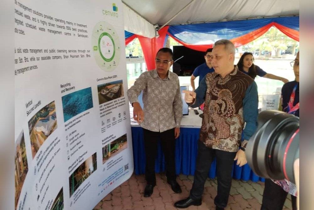 Wan Abdul Latiff (kiri) melihat maklumat berhubung pencemaran yang dipamerkan sempena Hari Alam Sekitar Negara 2023 di Hutan Bandar Majlis Bandaraya Iskandar Puteri (MBIP), Mutiara Rini pada Sabtu.