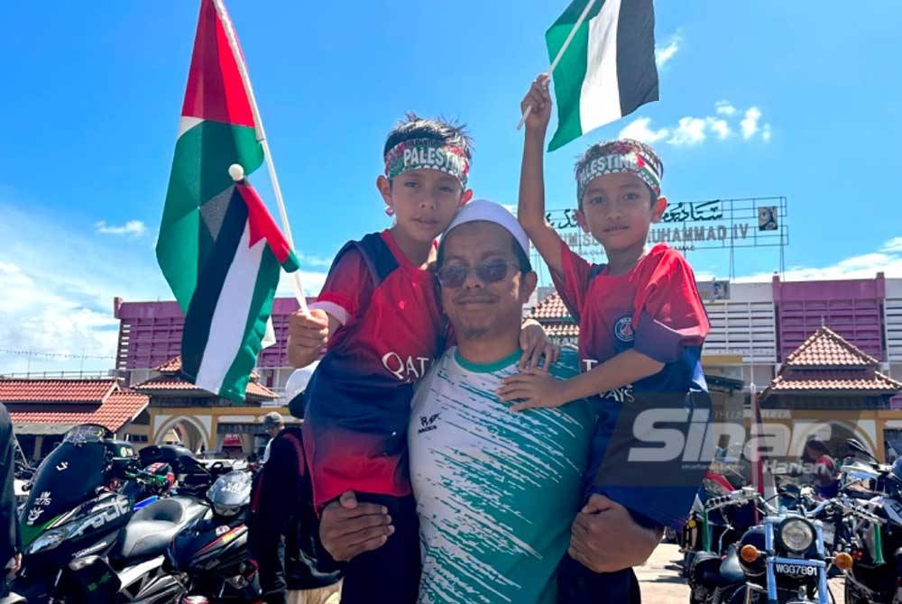 Mohd Khalis (tengah) mendukung kedua-dua anaknya sambil memegang bendera Palestin sebagai simbolik sokongan terhadap rakyat di negara itu pada Himpunan 2 Roda Untukmu Palestin 1.0 (Hiroup) di pekarangan Stadium Sultan Muhammad IV, di sini baru-baru ini.